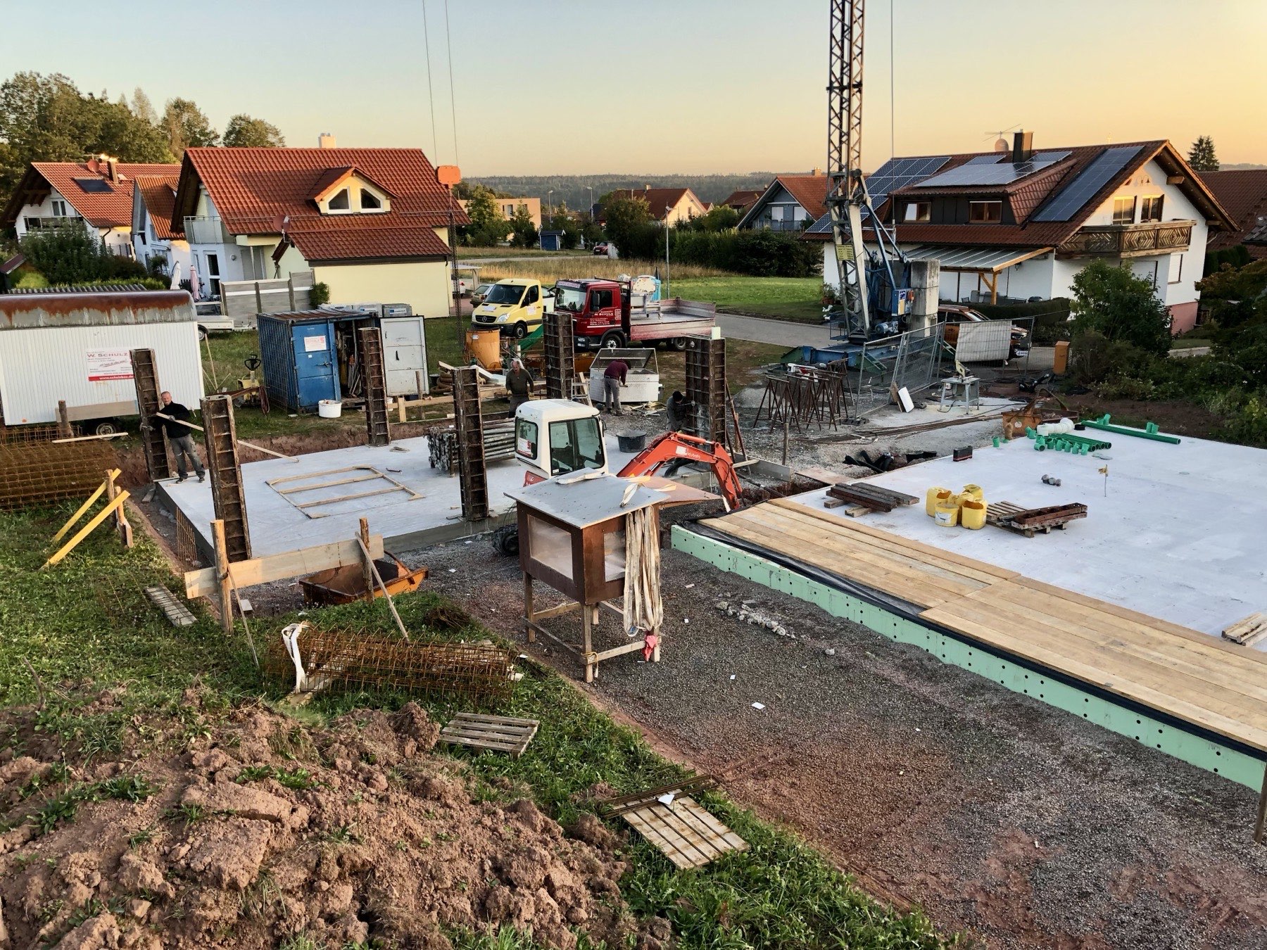 Rohbaustelle von SCHULZ-BAU im Abendlicht: Bodenplatte mit Wandschalung, Baukran und Einsatzfahrzeug